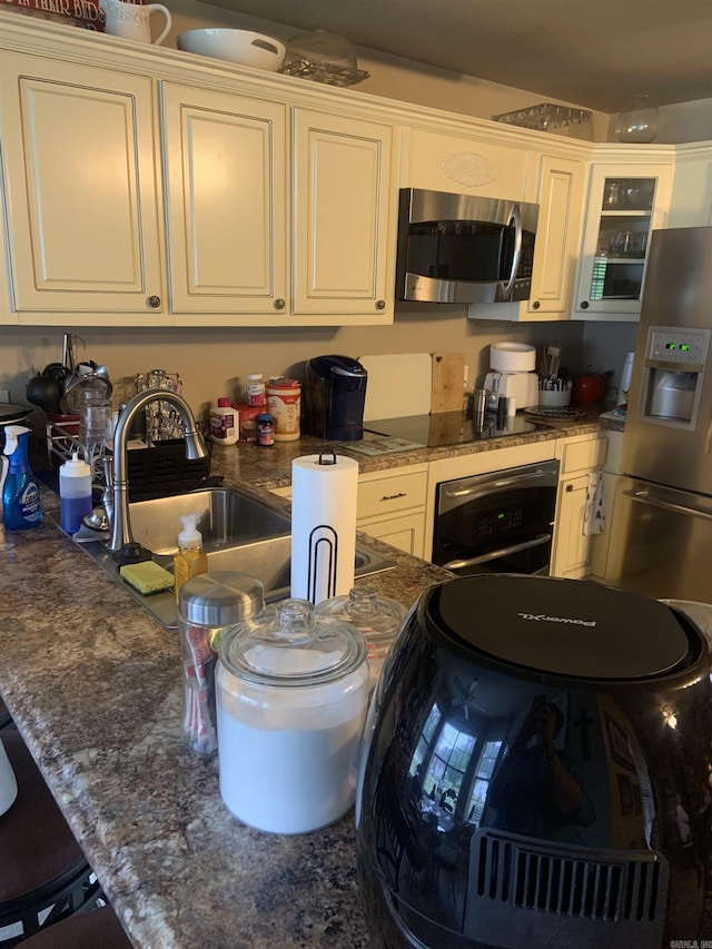 kitchen featuring appliances with stainless steel finishes, a sink, glass insert cabinets, white cabinetry, and a kitchen bar