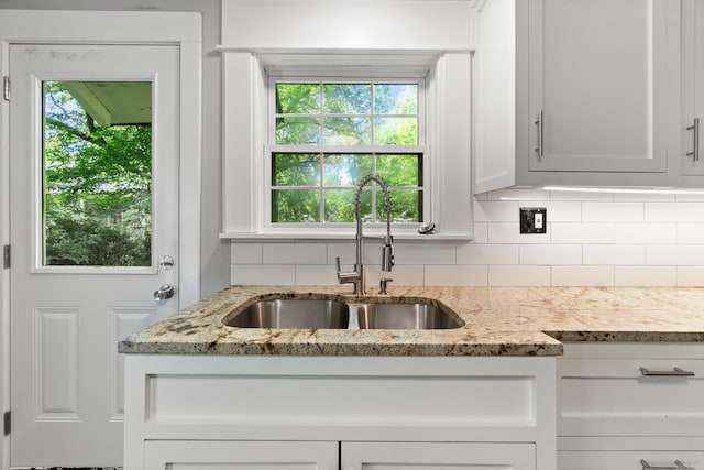kitchen with a sink, decorative backsplash, light stone countertops, and white cabinetry
