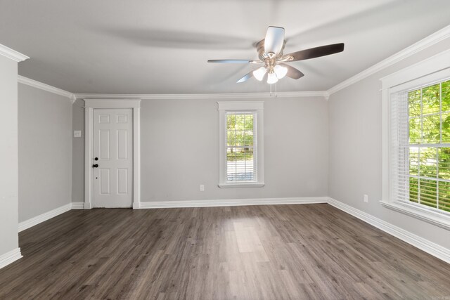 empty room featuring healthy amount of natural light, dark wood-type flooring, baseboards, and crown molding