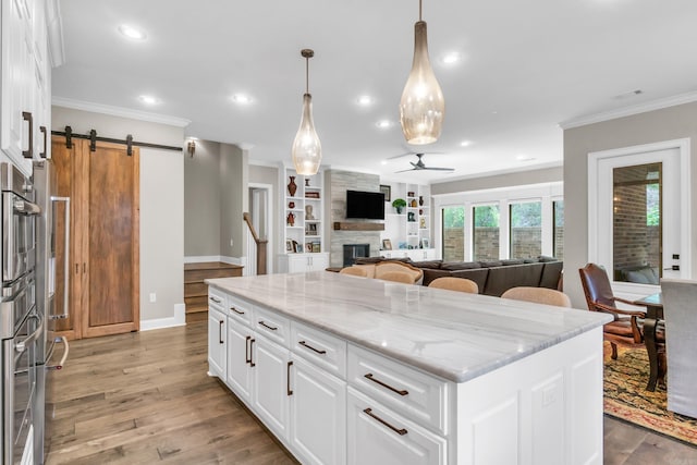 17 Cove Creek Pt, Little Rock, AR 72211 - kitchen with a ceiling fan, a barn door, ornamental molding, a center island, and light stone counters