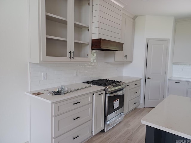 32 Propio Way, Hot Springs Village, AR 71909 - kitchen featuring stainless steel range with gas stovetop, wall chimney exhaust hood, decorative backsplash, light wood finished floors, and glass insert cabinets