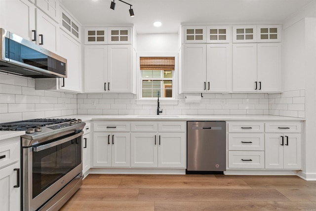 kitchen featuring stainless steel appliances, a sink, white cabinetry, light countertops, and tasteful backsplash