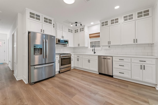 kitchen featuring stainless steel appliances, light wood-style flooring, white cabinetry, light countertops, and decorative backsplash