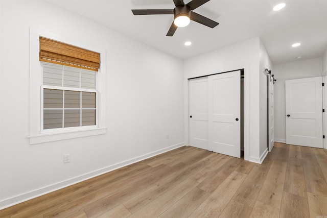 unfurnished bedroom with baseboards, light wood-style floors, recessed lighting, a barn door, and a closet