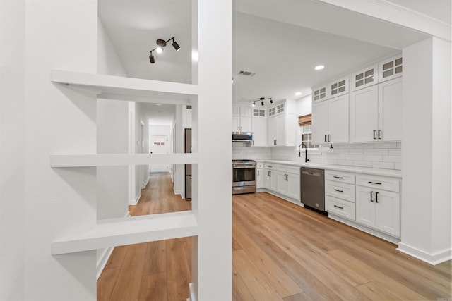 kitchen with appliances with stainless steel finishes, white cabinetry, decorative backsplash, light wood-style flooring, and glass insert cabinets