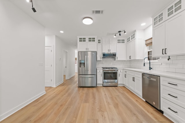 kitchen featuring stainless steel appliances, a sink, tasteful backsplash, white cabinets, and baseboards