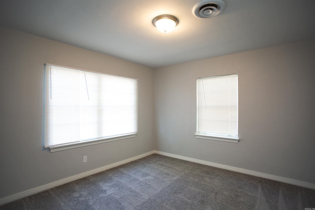 empty room featuring dark colored carpet and baseboards