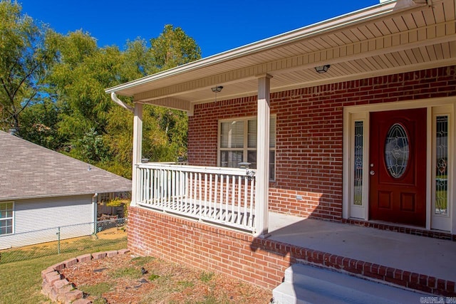 doorway to property with covered porch, brick siding, and fence