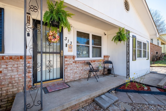property entrance with a porch and brick siding