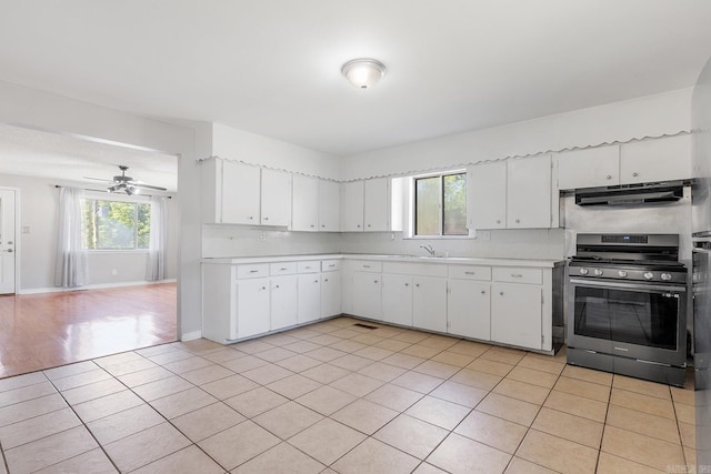 kitchen featuring stainless steel gas range, under cabinet range hood, light countertops, light tile patterned floors, and a ceiling fan