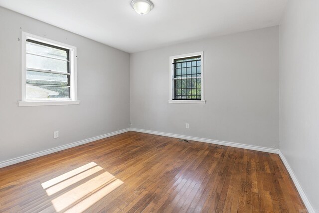 spare room featuring wood-type flooring, healthy amount of natural light, and baseboards