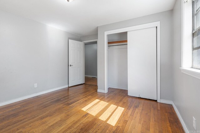 unfurnished bedroom featuring hardwood / wood-style flooring, baseboards, and a closet