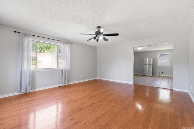 empty room featuring a textured ceiling, ceiling fan, light wood finished floors, and baseboards