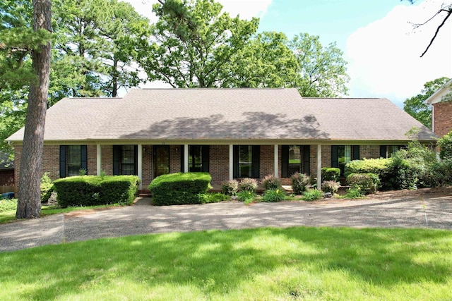 ranch-style home with brick siding, a front lawn, and roof with shingles