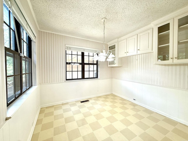 unfurnished dining area featuring a chandelier, light flooring, plenty of natural light, a wainscoted wall, and a textured ceiling