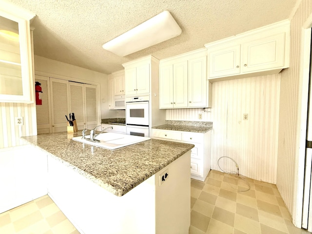 kitchen with white appliances, light floors, a sink, white cabinetry, and light stone counters