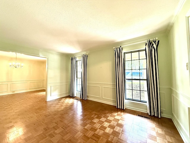 unfurnished room with a decorative wall, a chandelier, a textured ceiling, crown molding, and wainscoting