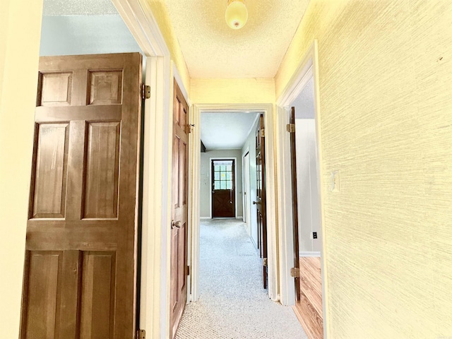 corridor with a textured ceiling, light colored carpet, and baseboards