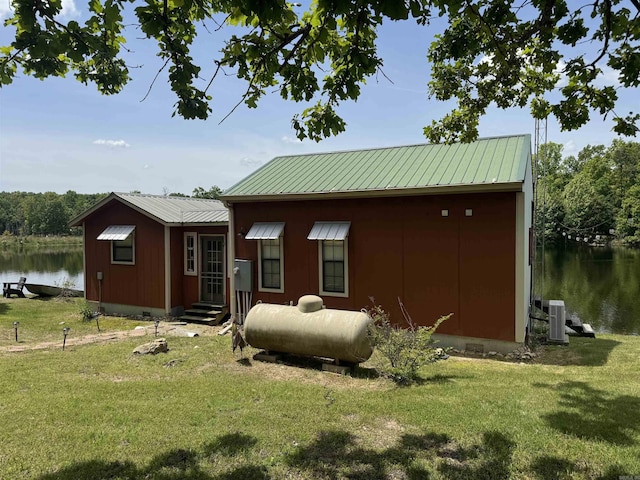 rear view of property with a yard, a water view, metal roof, and cooling unit