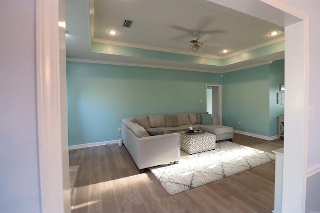 living room featuring crown molding, a tray ceiling, ceiling fan, wood finished floors, and baseboards