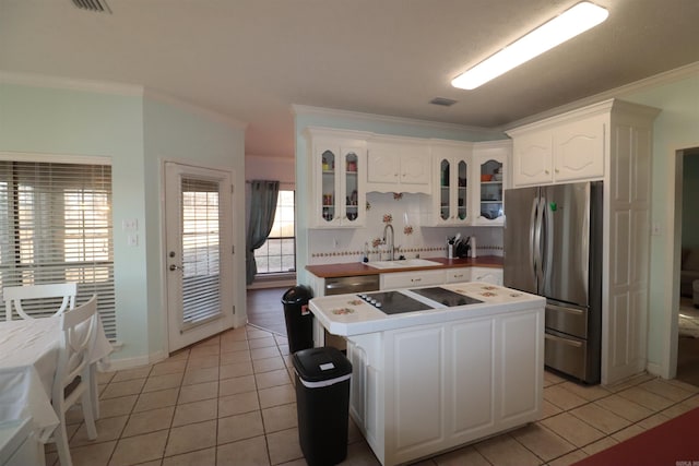 kitchen featuring stainless steel appliances, a sink, ornamental molding, light tile patterned floors, and glass insert cabinets