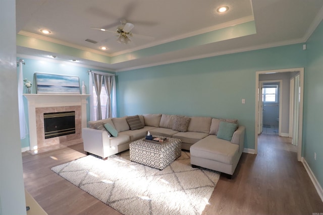living room featuring ornamental molding, ceiling fan, a tray ceiling, wood finished floors, and a tile fireplace
