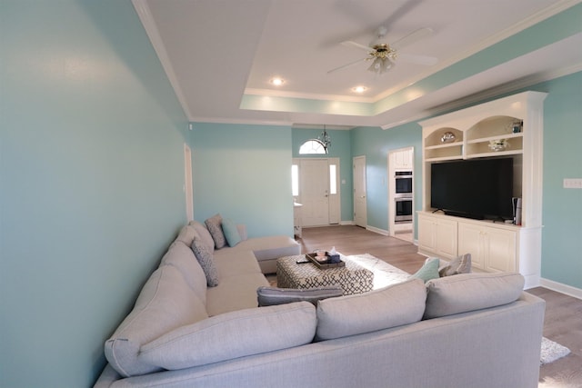 living area with light wood finished floors, ornamental molding, baseboards, a raised ceiling, and a ceiling fan