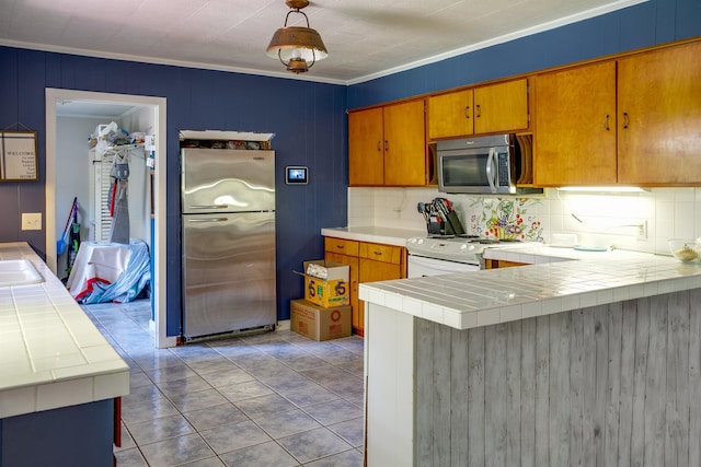 312 N E St, Harrisburg, AR 72432 - kitchen featuring appliances with stainless steel finishes, tile countertops, decorative backsplash, ornamental molding, and a peninsula