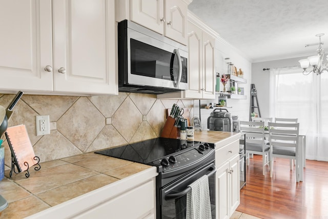 142 Peach St, Austin, AR 72007 - kitchen featuring stainless steel microwave, black electric range, tile counters, white cabinetry, and ornamental molding