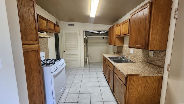 kitchen with a sink, white range with gas cooktop, under cabinet range hood, brown cabinets, and backsplash