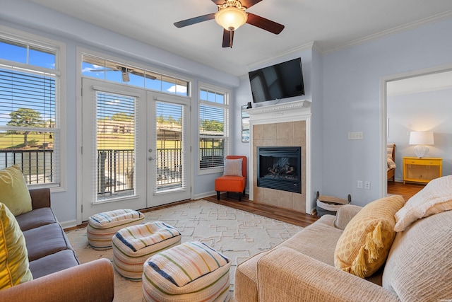 living area with a tiled fireplace, crown molding, a ceiling fan, wood finished floors, and baseboards