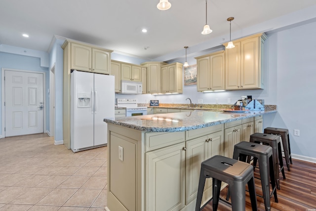 kitchen with cream cabinetry, white appliances, a peninsula, light stone countertops, and a kitchen breakfast bar