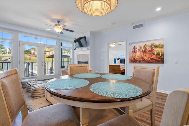 dining room with a ceiling fan, crown molding, light wood-style flooring, a tile fireplace, and french doors