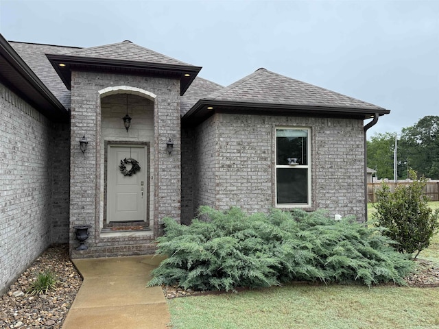 doorway to property featuring roof with shingles and brick siding