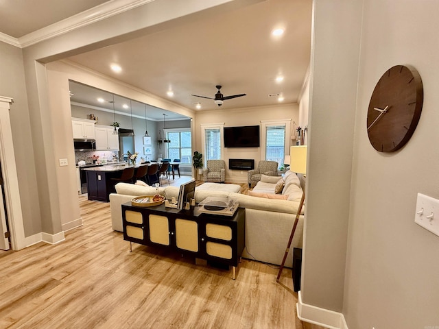 living room featuring ornamental molding, ceiling fan, light wood-style flooring, a fireplace, and baseboards