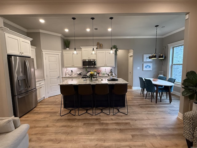 kitchen featuring stainless steel appliances, light stone counters, white cabinetry, decorative backsplash, and a center island with sink