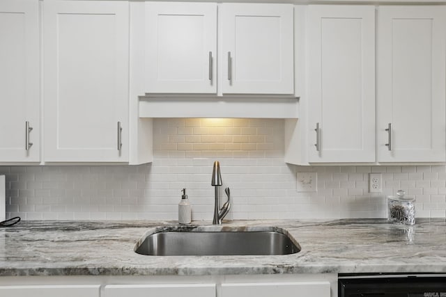 kitchen with a sink, white cabinetry, backsplash, light stone countertops, and dishwashing machine