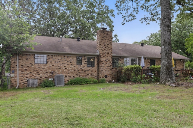 rear view of property featuring brick siding, central AC, a yard, and a chimney