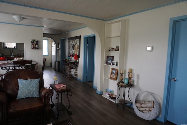 living room with arched walkways, dark wood-style flooring, built in shelves, and baseboards