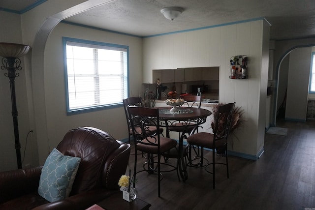 dining room featuring arched walkways, wood finished floors, ornamental molding, and baseboards
