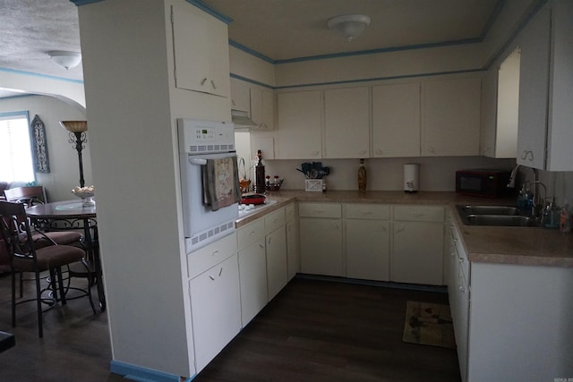kitchen featuring white oven, black microwave, dark wood-type flooring, a sink, and light countertops