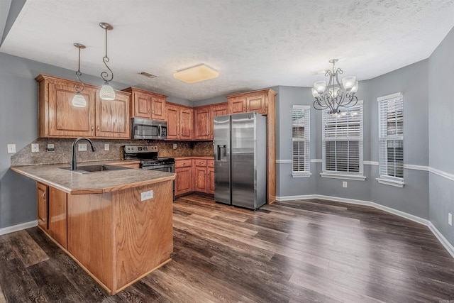 kitchen with appliances with stainless steel finishes, a sink, a peninsula, backsplash, and a chandelier