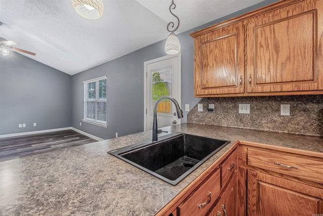 kitchen featuring a sink, lofted ceiling, wood finished floors, decorative backsplash, and ceiling fan