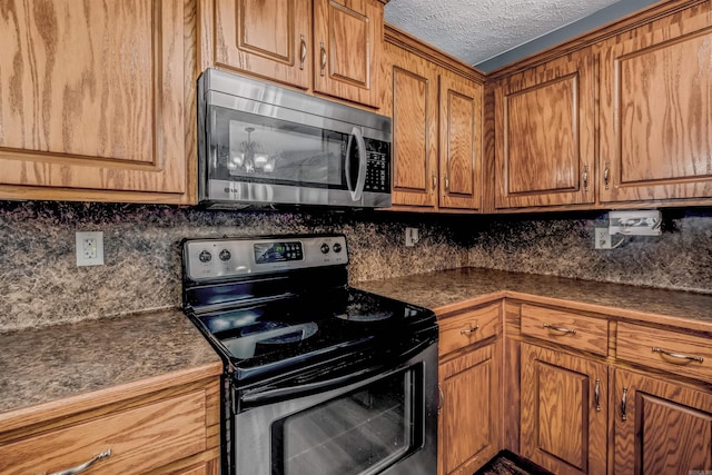 kitchen featuring appliances with stainless steel finishes, dark countertops, brown cabinets, tasteful backsplash, and a textured ceiling