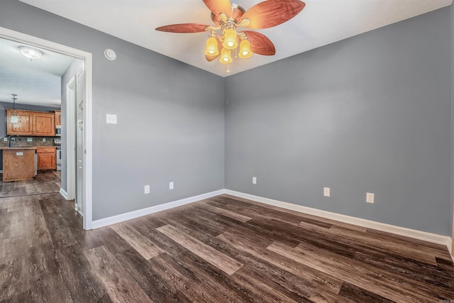 empty room featuring dark wood-type flooring, baseboards, ceiling fan, a sink, and a smoke detector