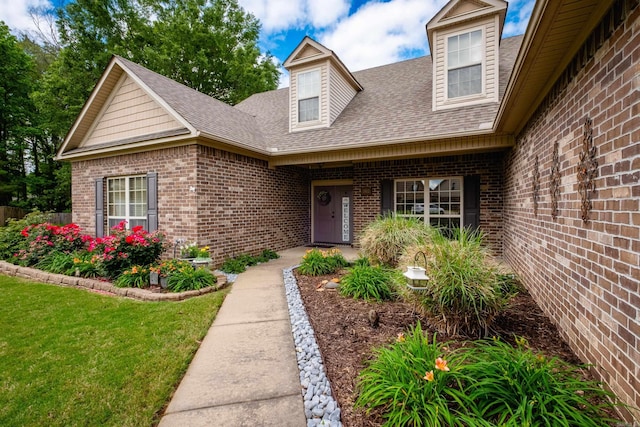 doorway to property featuring brick siding, a shingled roof, and a yard