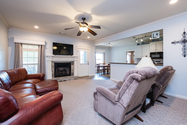 living area with a ceiling fan, crown molding, a fireplace, baseboards, and track lighting