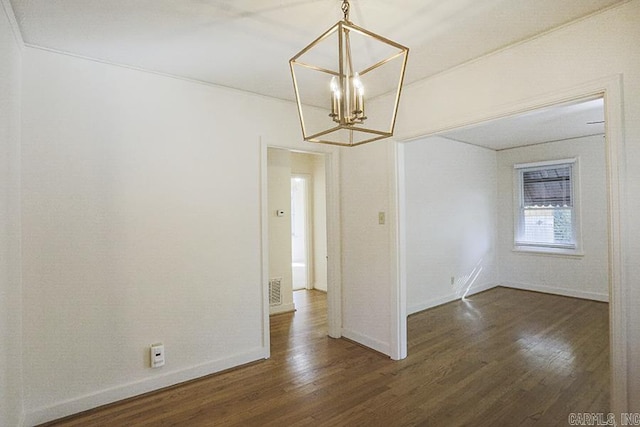 spare room featuring a chandelier, wood finished floors, and baseboards