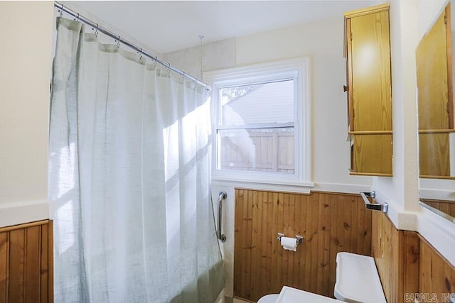 bathroom featuring toilet, wainscoting, curtained shower, and wooden walls