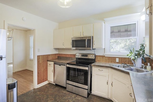 kitchen with stainless steel appliances, a sink, a wainscoted wall, white cabinetry, and wooden walls